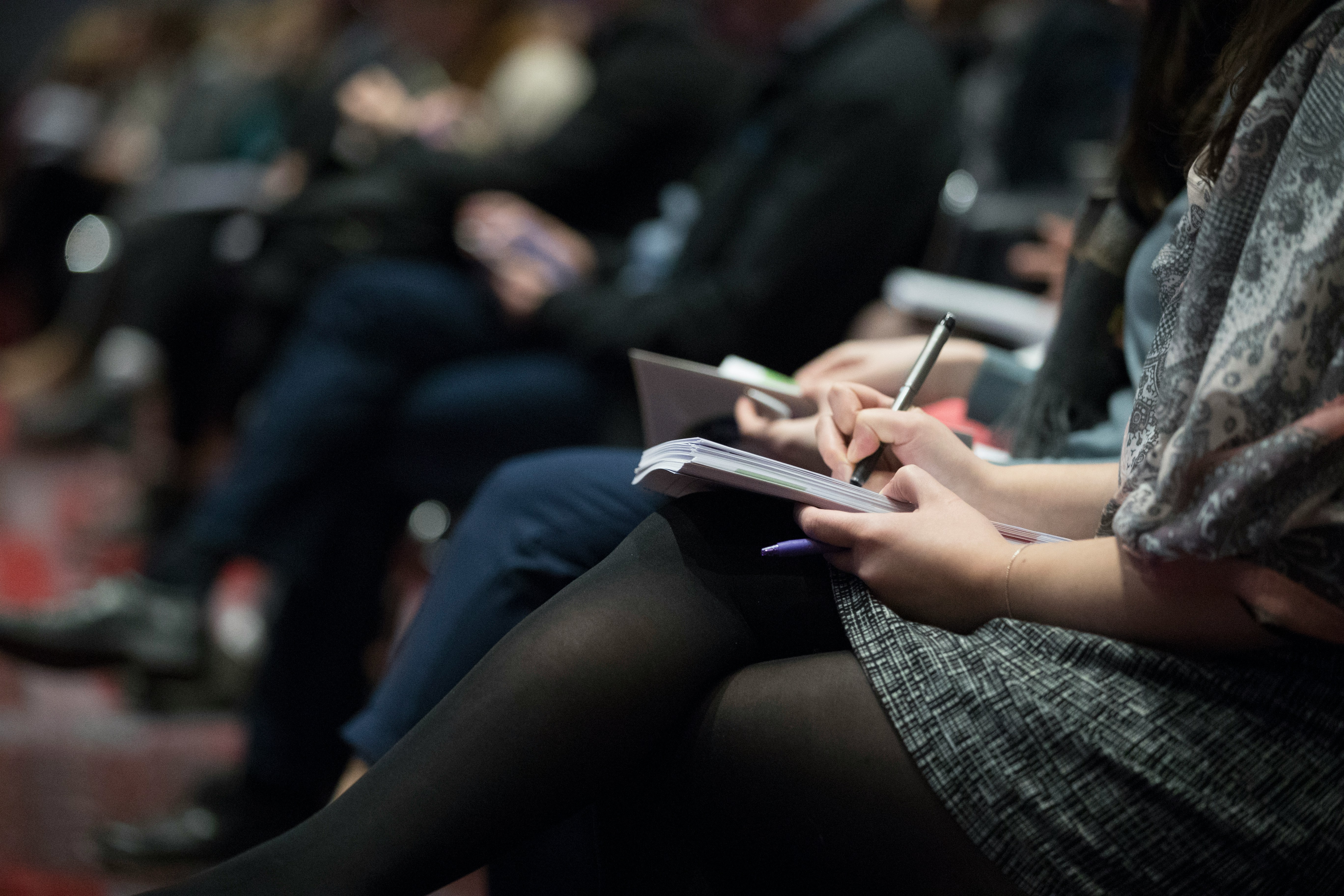 Close up of a woman taking notes in a seminar-styled setting.